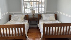 A room with two wooden beds, a small table with a lamp, and a window with blinds.