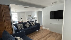 A modern living room with a dark blue sofa set, a flat-screen TV mounted on the wall, and a wooden floor.
