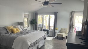 A bedroom with a large bed, a ceiling fan, a small table with a plant, a chair, and a view of the outdoors. - Northern Dream: All seasons lake house with nearby skiing, golfing and trails. (Gaylord)