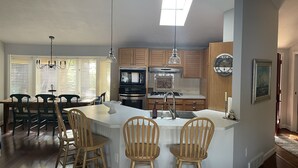 A modern kitchen with wooden cabinets, a central island with bar stools, a chandelier, and a ceiling fan. - Northern Dream: All seasons lake house with nearby skiing, golfing and trails. (Gaylord)