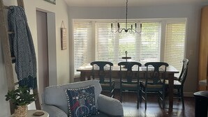 A living room with a blue armchair, a dining table with chairs, a chandelier, and a window with blinds. - Northern Dream: All seasons lake house with nearby skiing, golfing and trails. (Gaylord)