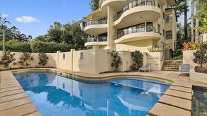 A modern building with a swimming pool, surrounded by a landscaped garden and a clear sky.