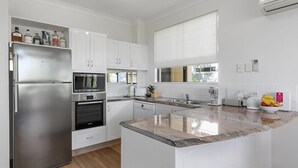 A modern kitchen with white cabinetry, stainless steel appliances, a granite countertop, and a window with blinds.