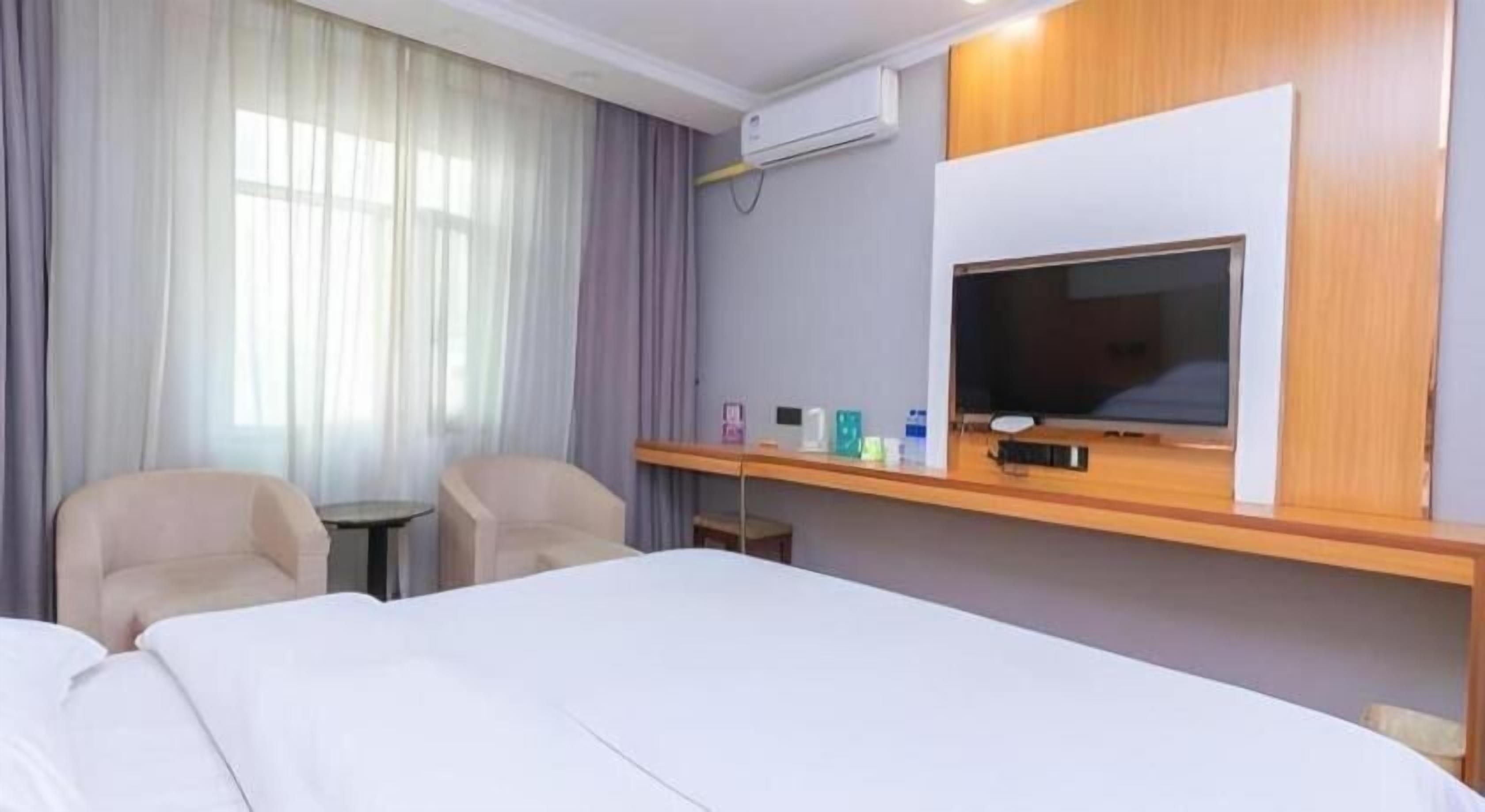 Habitación de hotel con cama, dos sillas, una mesita, televisor y equipo de aire acondicionado.