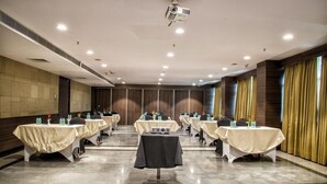 A conference room with multiple tables, each covered with a tablecloth, and equipped with water bottles and floral centerpieces. - Hide Away Suites (Noida)