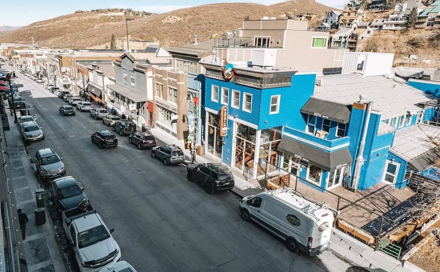 Vista da rua de uma cidade, com edifícios, carros estacionados e uma van.