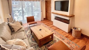 Un salon comprenant un canapé, un fauteuil, une table basse et un téléviseur à écran plat fixé au mur.