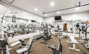A gym with various exercise equipment, a large mirror, and a carpeted floor.