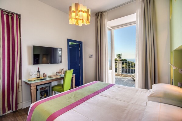 A hotel room with a bed, a desk with a computer, a TV, and a view of the outside. - Palazzo del Barone (Massa Lubrense)