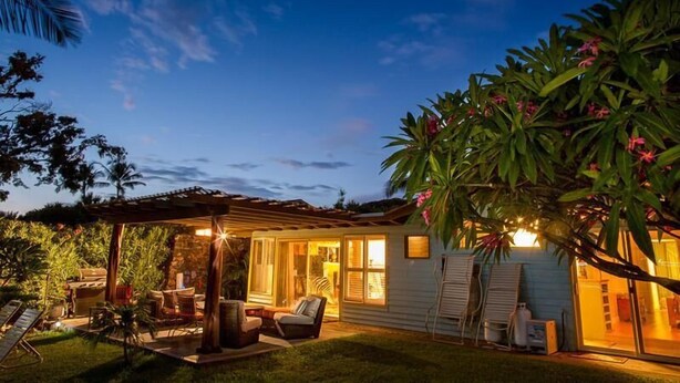 A house with a covered patio, outdoor seating, and a well-lit interior. - Hale Lani ~ Big Island Charmer with Panoramic Ocean Views ~ Near Best Beaches (Kamuela)
