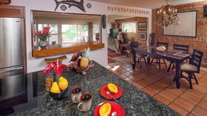 A kitchen with a granite countertop, a refrigerator, and a dining area with a table and chairs. - Hale Lani ~ Big Island Charmer with Panoramic Ocean Views ~ Near Best Beaches (Kamuela)