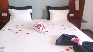Un letto rifatto con cuscini bianchi e scuri, un bouquet di fiori e petali di rosa sparsi.