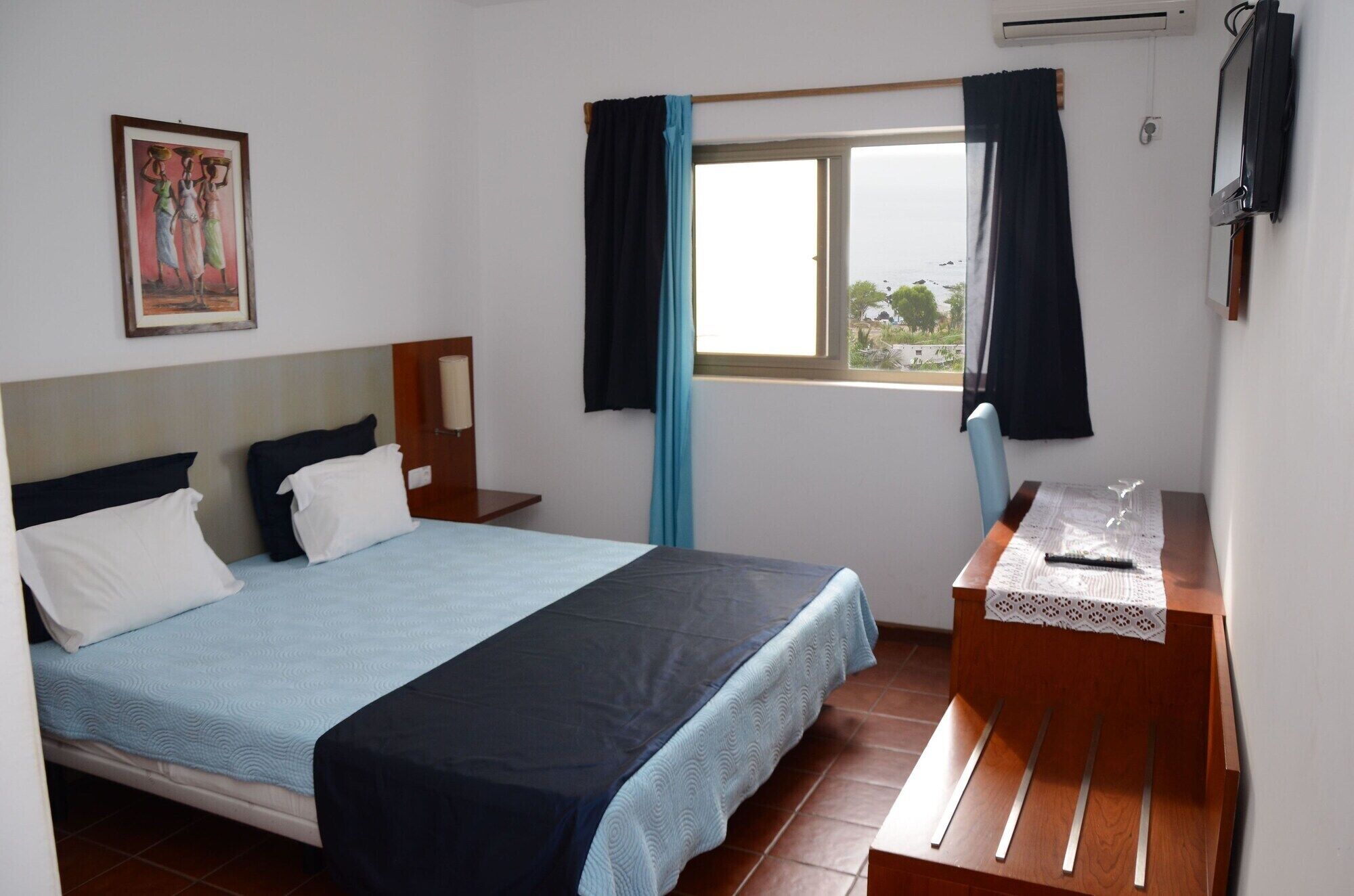 Een hotelkamer met een bed, een bureau, een raam met gordijnen en een schilderij aan de muur.