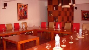 Una sala conferenze con tavoli in legno e sedie rosse, dotata di bottiglie d'acqua e bicchieri da vino.