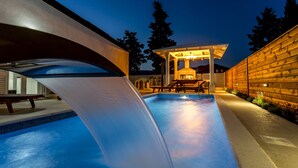 Una piscina con una cascada, un espacio de descanso techado y un muro de madera.