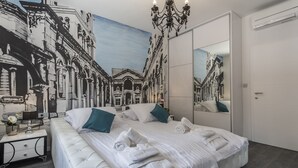 Una habitación de hotel moderna con una cama grande, una mesita de noche, un espejo y un mural con una escena callejera en la pared.