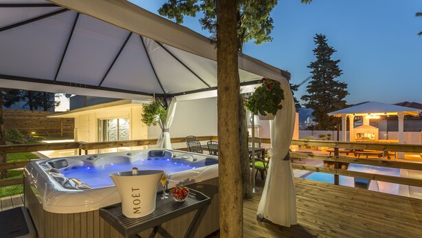 Un jacuzzi con un balde y una copa de vino, una terraza de madera y una zona cubierta con dosel.