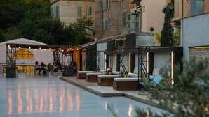 Ein Terrassenbereich im Freien mit Sitzgelegenheiten und einem überdachten Bereich, umgeben von Gebäuden.