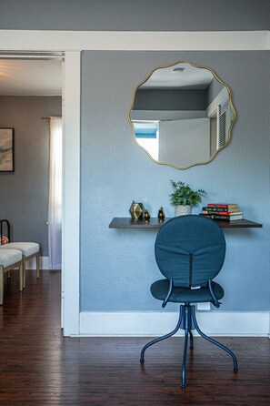 A room with a dark wooden floor, a blue chair with a black metal base, a white door, and a wall-mounted mirror with a gold frame.