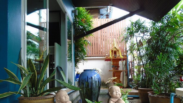 Un patio con macetas, un jarrón azul grande y dos estatuas de Buda.