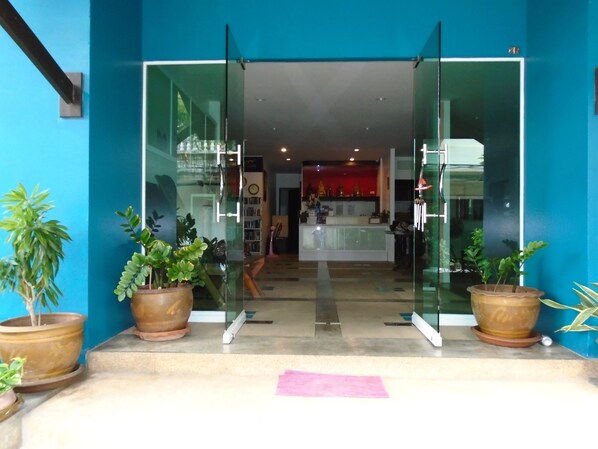 Un espace d’accueil doté de portes vitrées, de plantes en pot et d’un comptoir bien visible, avec un fond rouge.