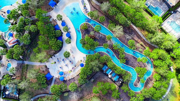Luchtbeeld van een resort met een kronkelend zwembad, ontspanningsruimtes en weelderige begroeiing.