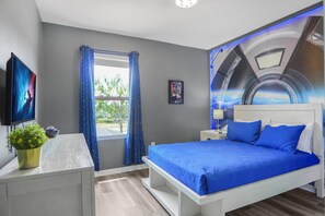 Un dormitorio con cama, televisión, ventana con cortinas y un mural en la pared.