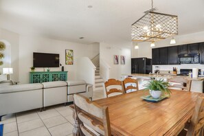 Una sala de estar moderna con un sofá, una mesa de comedor de madera con sillas, un televisor y una escalera que lleva a la cocina.
