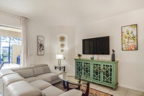 Ein Wohnzimmer mit einer Couch, einem Glastisch, einem grünen Schrank, einem Fernseher und einem Gemälde an der Wand.