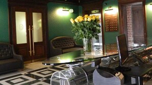 A lobby with a glass table, a vase of yellow flowers, a tufted armchair, and a patterned floor. - Palazzo Rosso (Poznań)