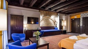 A hotel room with a wooden ceiling, a brick wall, a sofa, a bed, a desk, and a chair. - Palazzo Rosso (Poznań)