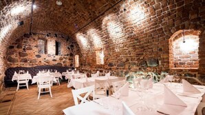 A restaurant with stone walls and brick ceiling, white tables and chairs, and a herringbone floor pattern. - Palazzo Rosso (Poznań)