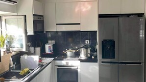 A modern kitchen with white cabinets, a stainless steel refrigerator, a built-in oven, and a black countertop.