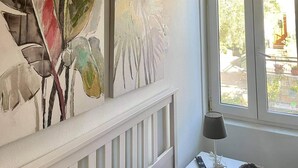 A room with a white ceiling, a window with a view of greenery outside, and two abstract leaf paintings on the wall.
