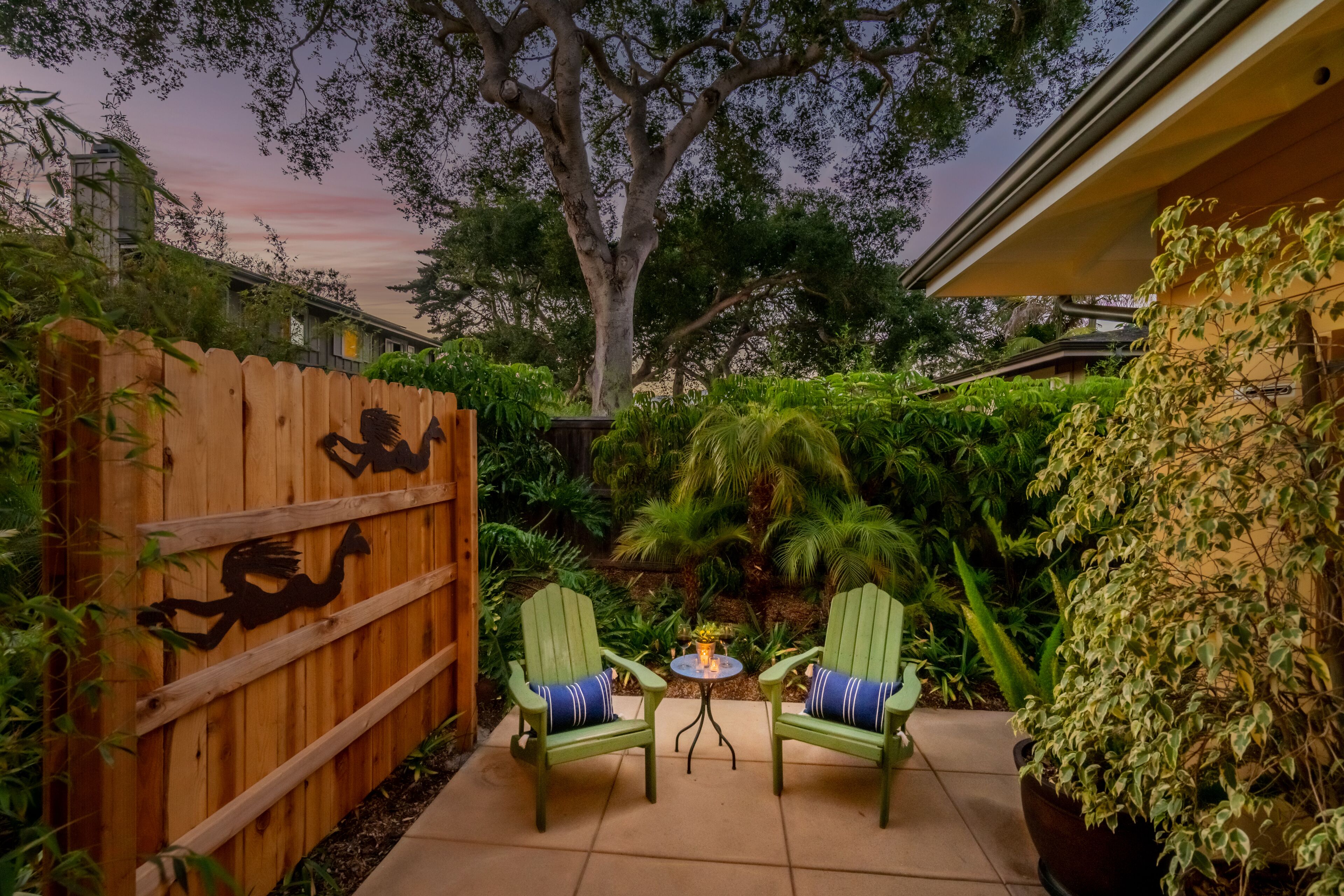 A patio with two green Adirondack chairs, a small round table, and a wooden fence with a decorative cutout.