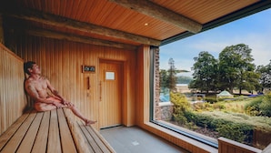 A sauna room with wooden benches, a large window, and a view of a landscaped garden. - Lodore Falls Hotel (Keswick)