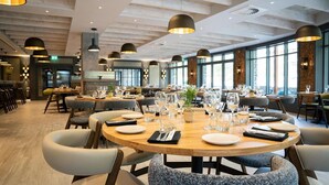 A modern restaurant with round tables set for dining, large windows, and pendant lighting. - Lodore Falls Hotel (Keswick)