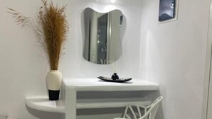 Un bany amb un moble blanc, un mirall, una cadira blanca i un vas decoratiu amb plantes seques.