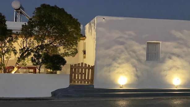 Un edifici amb façana blanca, tanca de fusta i dues finestres il·luminades.