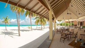 Un restaurante frente a la playa con terraza, palmeras y vista al océano.