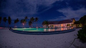 Propiedad frente al mar con piscina, palmeras y un edificio de techo inclinado.