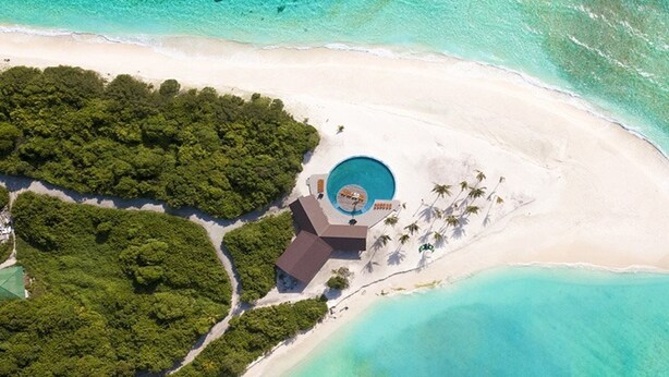 Vista aérea de un resort con piscina central, rodeado de exuberante vegetación y una playa de arena.