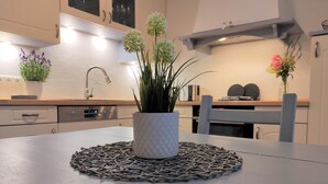 Une cuisine avec une table placée au centre, surmontée d’un set de table en fibres tressées, une plante en pot et un four à micro-ondes en arrière-plan.
