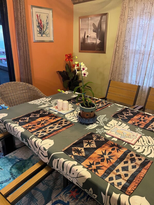 Un comedor con una mesa cubierta por un mantel estampado, una orquídea en maceta y un cuadro en la pared.