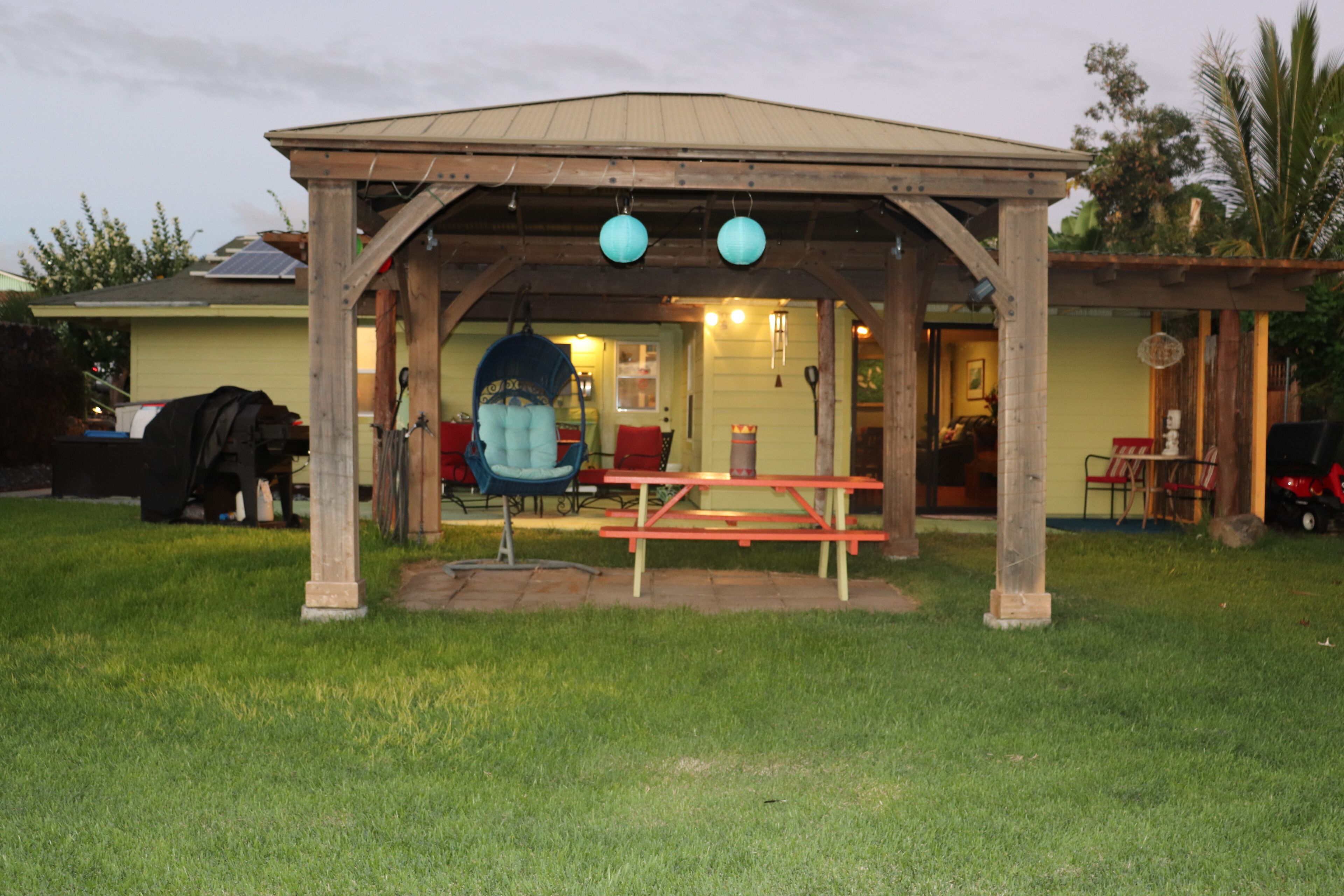 A covered outdoor seating area with a picnic table and a hanging chair.