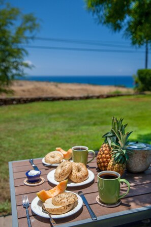 Una mesa de picnic con comida y bebidas, una piña, y vista al océano.