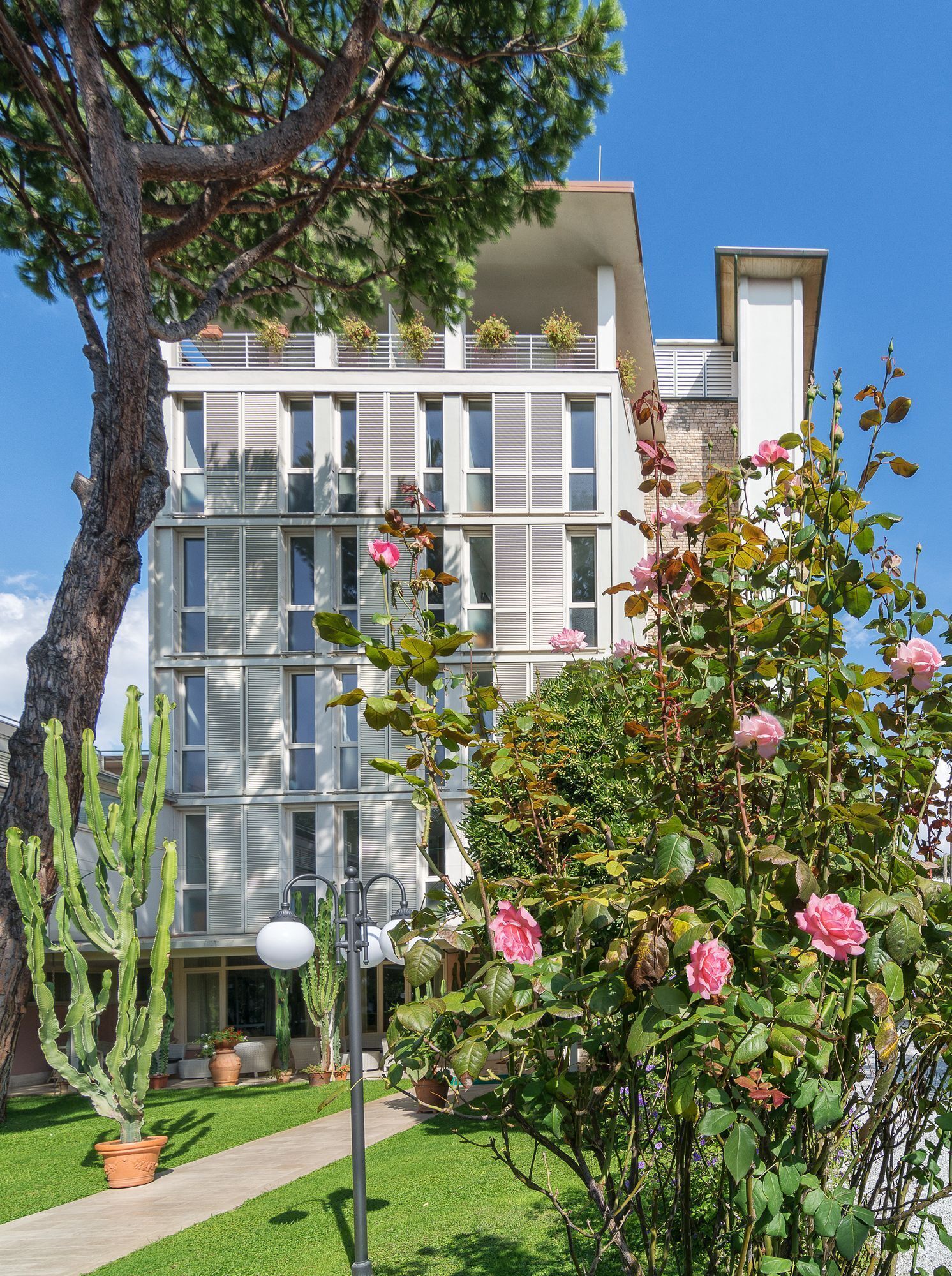 A modern building with a flat roof, large windows, and balconies with plants.