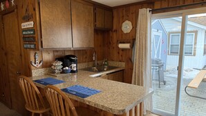 Una cucina con armadietti in legno, una macchina da caffè e un lavello. Sul bancone ci sono due sedie di legno e un sottopiatti blu.