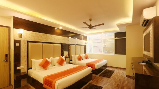A hotel room with two beds, a ceiling fan, a large window, and a mirror. - Plazzo (New Delhi)