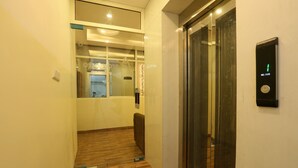 A hallway with a wooden floor, a glass elevator door, and a welcome sign on the wall. - Plazzo (New Delhi)